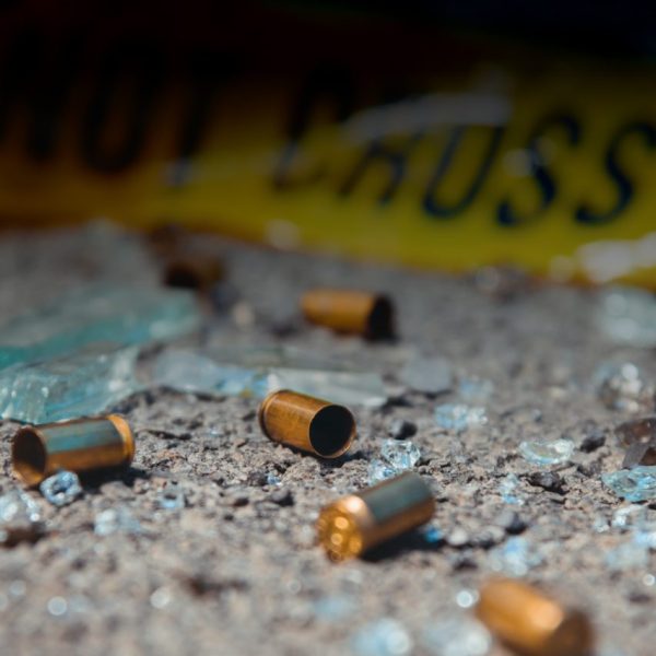 Photo of shell casings and broken glass in front of some "Do Not Cross" police tape.